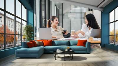 Two female colleagues share a light-hearted moment with coffee during a casual office meeting. Wall mural