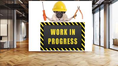 pug dog wearing yellow constructor safety helmet,holding pliers and screwdriver, with warning sign saying work in progress, isolated on white background Wall mural