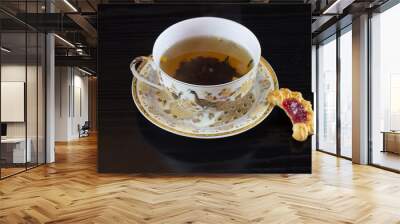  White cup in golden brown patterns of hot tea with homemade biscuit-based saucer  isolated on black background  Wall mural