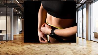 Close up of young woman with slender body measuring waist with tape after morning workout at gym. Fitness lady with bare torso estimating new forms of her figure. Wall mural