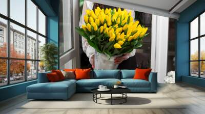 Yellow color tulips in woman hand. Young beautiful woman holding a spring bouquet. Bunch of fresh cut spring flowers in female hands. Flowers shop concept Wall mural