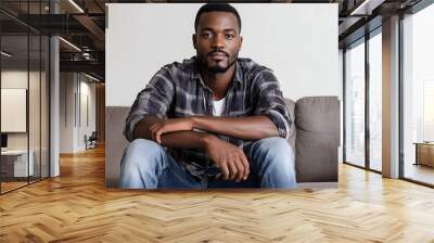 photogenic handsome african american man in casual attire with serious face expression sitting on sofa Wall mural