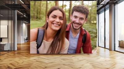 A young adult couple smiling to camera during a hike in a forest, close up portrait Wall mural