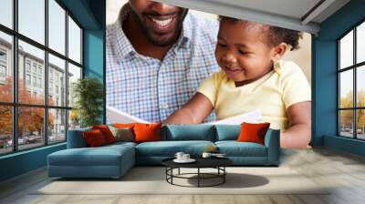 Baby Daughter And Father Sitting On Sofa Reading Book Together Wall mural