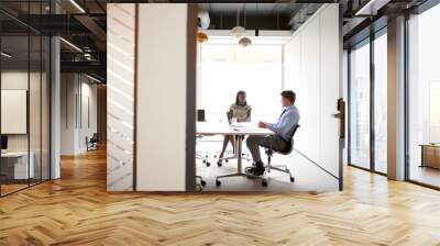 Businessman And Businesswoman Having Discussion Around Boardroom Table Viewed Through Meeting Room Door Wall mural