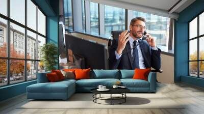 Businessman Making Phone Call Sitting At Desk In Office Wall mural