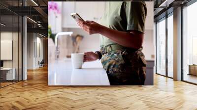 Close Up Of American Female Soldier In Uniform In Kitchen On Home Leave With Mobile Phone Wall mural