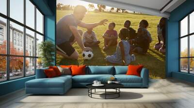 Elementary school kids and teacher sitting with ball in field Wall mural