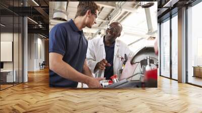 Engineer talking to male apprentice at his workstation, low angle Wall mural