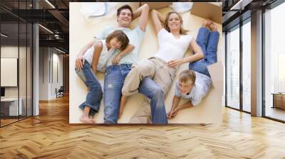 Family lying on floor by open boxes in new home smiling Wall mural