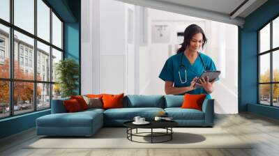 Female Doctor Wearing Scrubs In Hospital Corridor Using Digital Tablet Wall mural