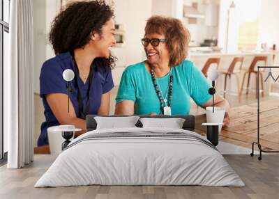 Female healthcare worker sitting at table smiling with a senior woman during a home health visit Wall mural