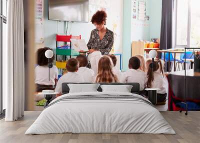 Female Teacher Reading Story To Group Of Elementary Pupils Wearing Uniform In School Classroom Wall mural