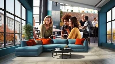 Four Young Female Friends Meeting Sit At Table In Coffee Shop And Talk Wall mural