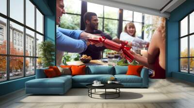 Group Of Friends Sitting Around Table At Home For Christmas Dinner Pulling Crackers Wall mural