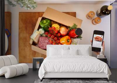 Hand In Kitchen Holding Phone With Recipe On Screen For Online Food Recipe Kit Delivered To Home Wall mural