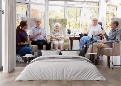 Male And Female Residents Sitting In Chairs And Talking With Carer In Lounge Of Retirement Home Wall mural