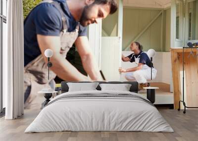 Male Carpenter With Female Apprentice Measuring Wood To Build Outdoor Summerhouse In Garden Wall mural