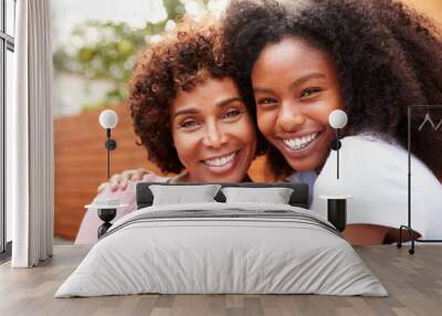 Middle aged black mum and teenage daughter embracing and smiling to camera Wall mural