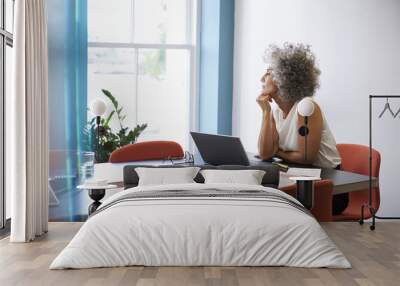 Middle aged woman looking out of the window in the boardroom Wall mural