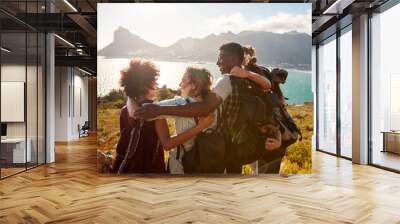 Millennial friends on a hiking trip embrace at the summit to celebrate their climb, back view Wall mural