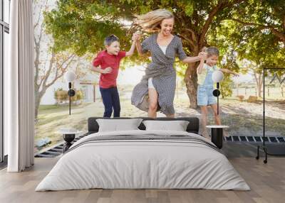 Mother Playing With Children On Outdoor Trampoline In Garden Wall mural