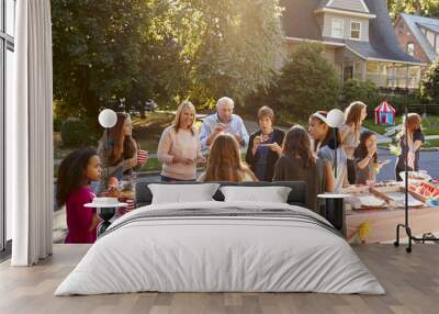 Neighbours talk and eat around a table at a block party Wall mural