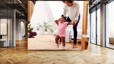 Parents At Home Encouraging Baby Daughter To Take First Steps Wall mural