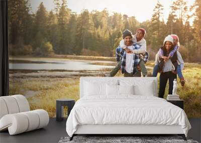 Parents Giving Children Piggyback Ride On Walk By Lake Wall mural