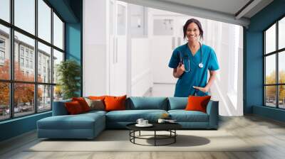 Portrait Of Smiling Female Doctor Wearing Scrubs In Hospital Corridor Holding Digital Tablet Wall mural