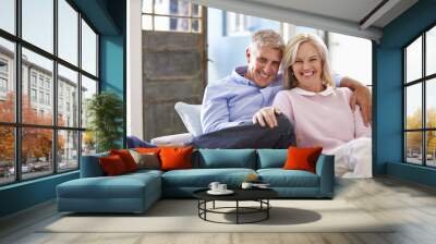 Portrait Of Smiling Mature Couple Sitting On Sofa At Home Wall mural