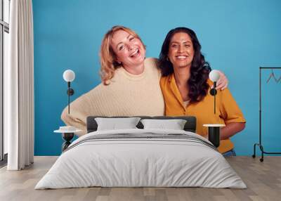 Portrait Of Two Mature Female Friends Laughing At Camera Against Blue Background Wall mural