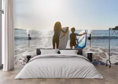 Rear View Of Two Children Wearing Wetsuits Running Into Sea With Bodyboards On Beach Vacation Wall mural