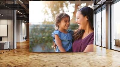 Smiling Hispanic Mother Holding Daughter Laughing In Garden At Home Wall mural