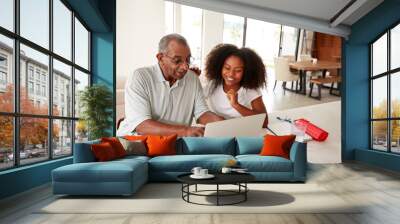 Smiling teenage black girl sitting at home helping her grandfather use a laptop computer Wall mural