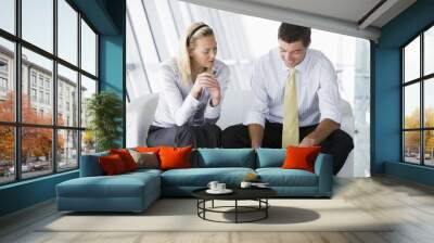 two businesspeople sitting in office lobby talking and smiling Wall mural