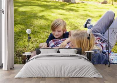 Two kids playing with their dad, lying in a park, side view Wall mural