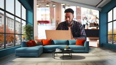 Young Businessman Sitting At Desk With Laptop In Modern Open Plan Office Wall mural