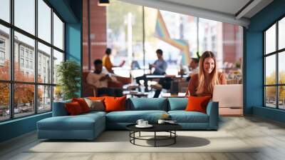 Young Businesswoman Sitting At Desk Writing In Notebook In Modern Open Plan Office Wall mural