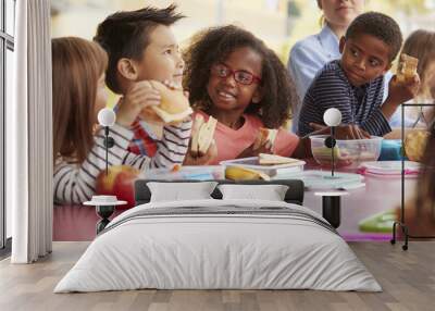 Young school kids eating lunch talking at a table together  Wall mural