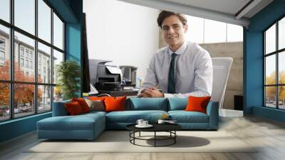 Young white businessman at an office desk, smiling to camera Wall mural