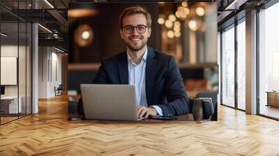 Young smiling blond Caucasian man sitting at desk using laptop. Happy busy professional businessman manager working on computer corporate technology in office. Wall mural