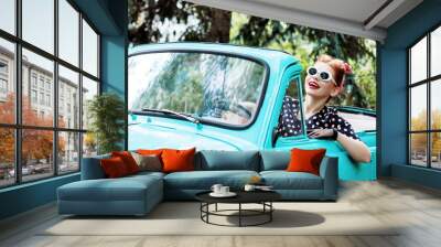 Beautiful stylish woman in vintage bright dotted clothes and glasses is driving mint old car after shopping. Fashion pin-up girl is travelling by auto. Retro style concept. Vacation trip mood. Wall mural