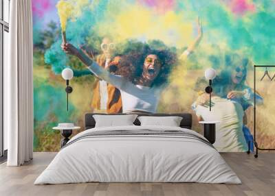 Beautiful young man and woman hold light up colored smoke bombs - Happy friends having fun in the park with multicolored smoke bombs - Young students celebrating spring break together. Holi festival. Wall mural