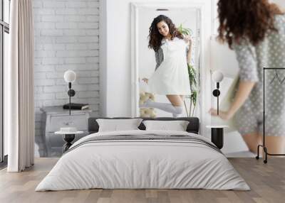 Young beauty girl woman female in grey shorts and white top pajamas sleepwear choosing dress clothes to wear in front of mirror in interior bedroom with grey bedside table. Morning weak up concept. Wall mural