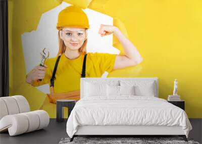 Young blond woman in uniform builder clothes, hardhat is holding metal wrench. Girl worker is looking confident. Repair, building at home, flat concept. Instruments, tools, accessories for renovation. Wall mural