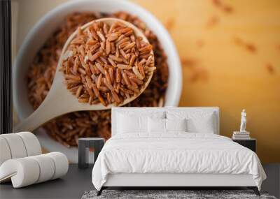 Closeup brown rice or red rice with wooden spoon and white ceramic bowl on wood table top. Healthy organic food concept. Wall mural