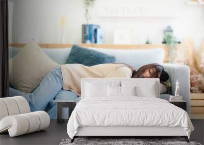 Asian woman resting at home on couch, feeling exhausted after work, lacking energy, or overworked, too tired, and lacking motivation Wall mural