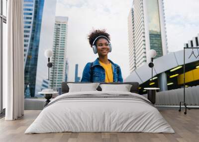 Cheerful black student girl wearing headset and using mobile smartphone, Walking at college building outdoor, Happy and smiling woman teenager. Modern education Wall mural