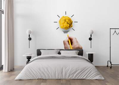 Creative thinking ideas and innovation concept. Paper scrap ball yellow colour with light bulb symbol on white background and hand holding yellow pencil Wall mural